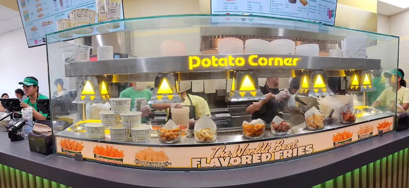 Staff prepare flavored fries behind a Potato Corner counter