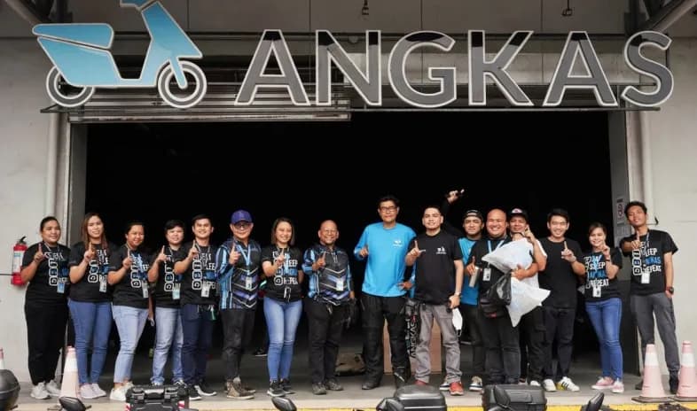 A group of Angkas riders in uniform standing in front of an Angkas sign